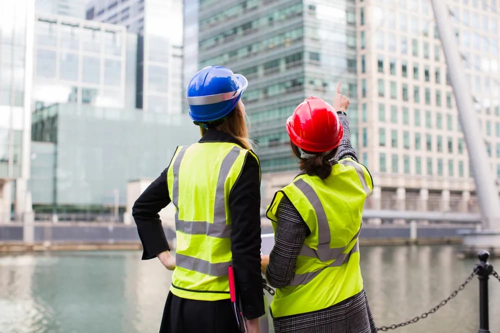 Two construction professionals in hard hats and high-visibility vests reviewing a building development on site