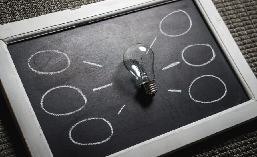 A lightbulb placed on a chalkboard with several chalk-drawn circles and connecting lines, suggesting a brainstorming or idea flow concept.