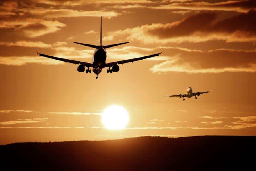 Two airplanes are flying close to sunset, with one preparing to land and the other in the distance. The scene features an orange sky with scattered clouds and a setting sun, reminiscent of heads finalizing purchase orders as another day wraps up.