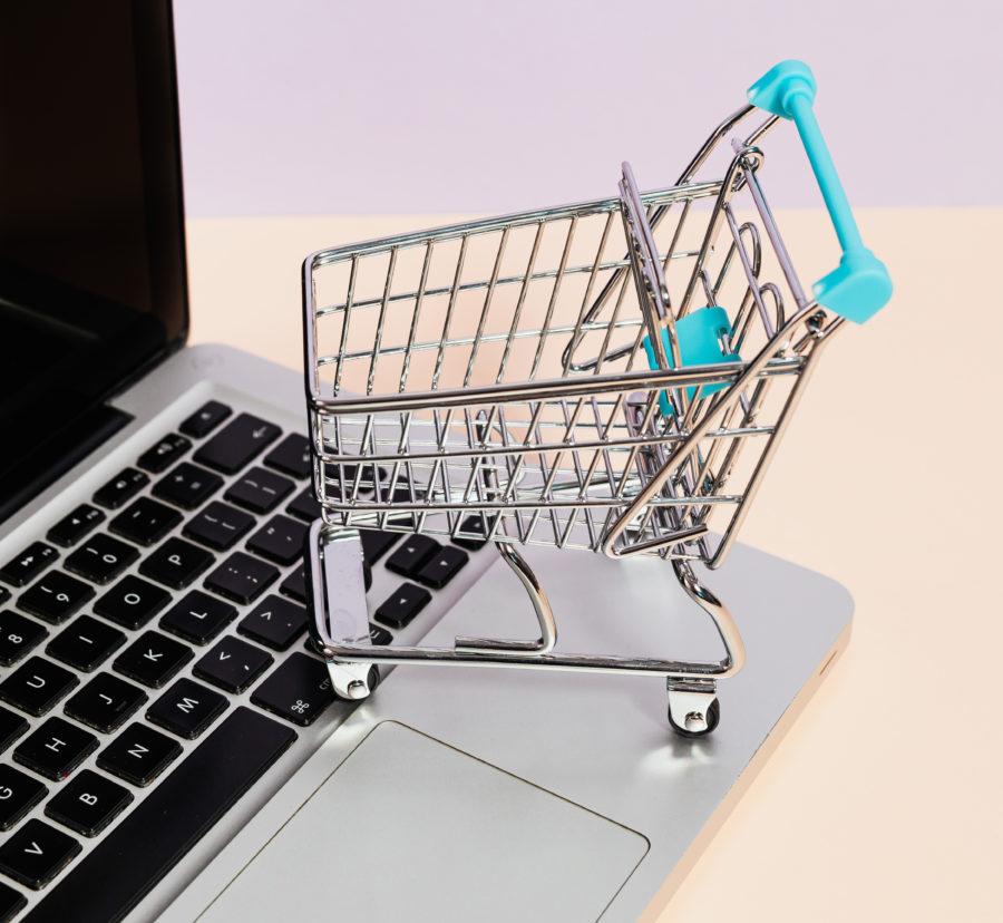 A miniature shopping cart sits atop a laptop keyboard, symbolizing online purchasing.