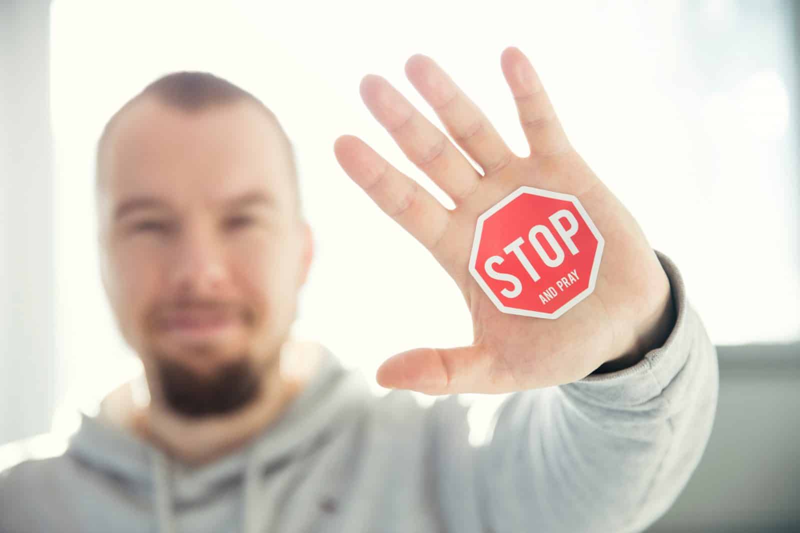 Man holding up his hand with a red stop sign sticker that says "STOP and PRAY.