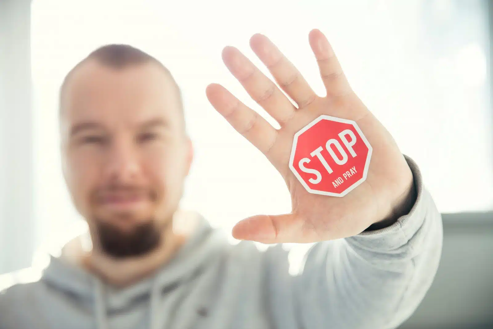 Man holding up his hand with a red stop sign sticker that says "STOP and PRAY.
