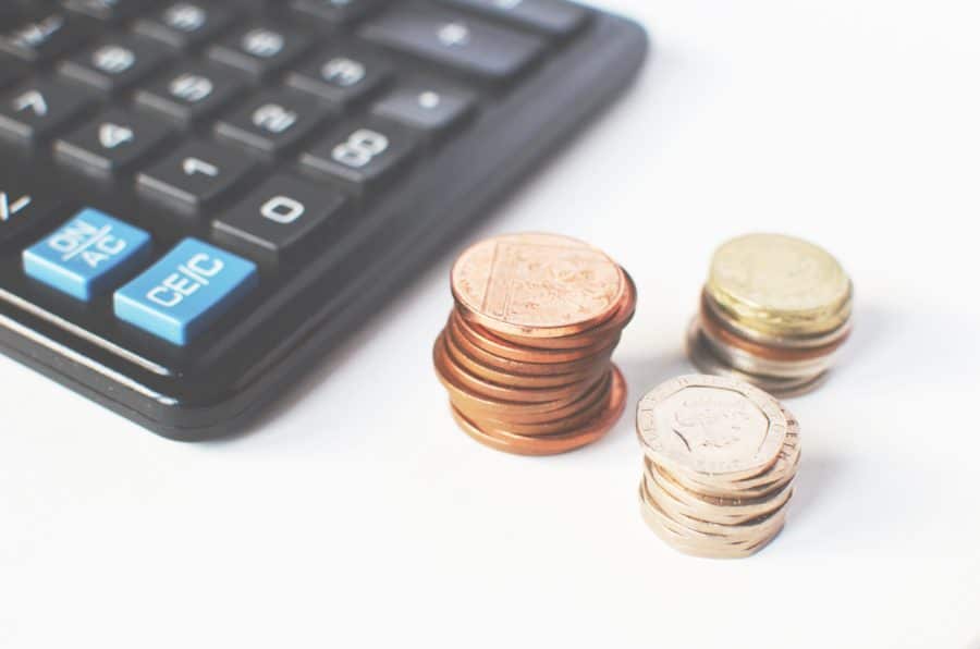 A close-up of a calculator next to piles of coins in various denominations on a white surface.
