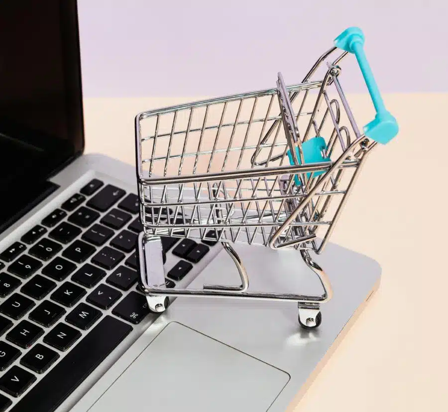A miniature shopping cart sits atop a laptop keyboard, symbolizing online purchasing.