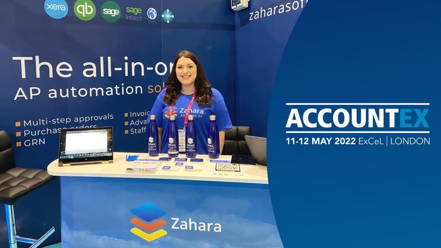 A woman stands at the Zahara booth at ACCOUNTS 2022, ExCeL London. The Accountex booth highlights AP automation solutions with various promotional materials on display, including a laptop, pamphlets, and water bottles.